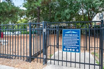 A sign for dog park rules is posted on a fence.